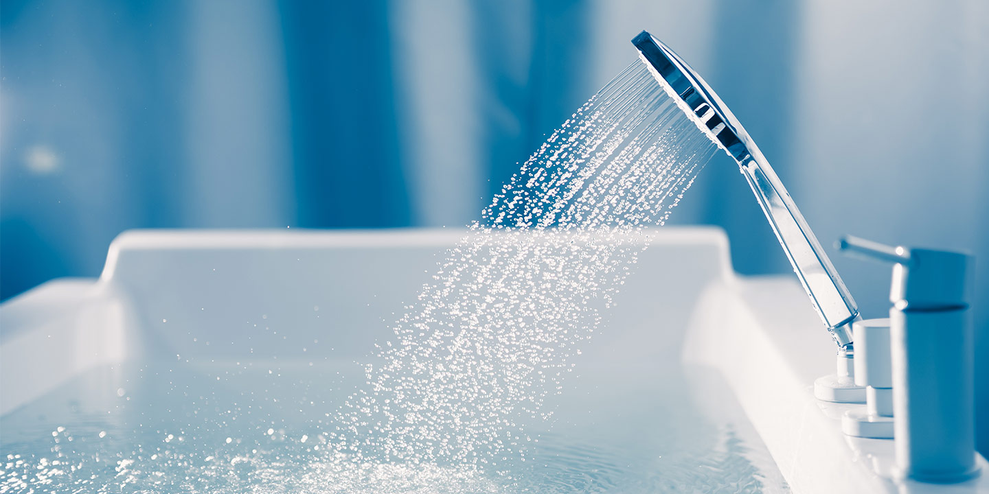 Hand shower running over a clean white bathtub
